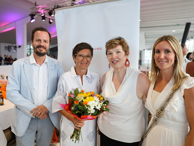 Vier Personen posieren gemeinsam, eine hält Blumen in der Hand.