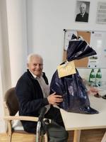 Ein älterer Mann sitzt an einem Tisch mit einem großen Geschenk in den Händen.