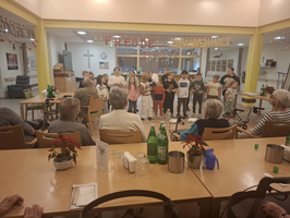 Kinder singen vor Senioren in einem Gemeinschaftsraum mit weihnachtlicher Dekoration.