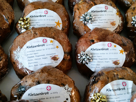 Mehrere Kletzenbrote mit Etiketten und dekorativen Schleifen auf einem Tisch.