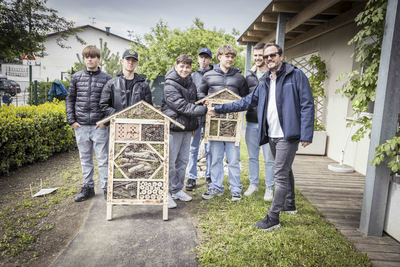 Sechs Jugendliche und ein Erwachsener präsentieren Insektenhotels im Freien.