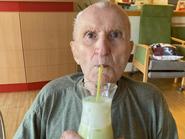Ein älterer Mann hält ein Getränk mit einem Strohhalm in der Hand.