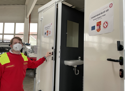 Ein Sanitäts- und Hygienetrailer mit einem Helfer im roten Outfit.