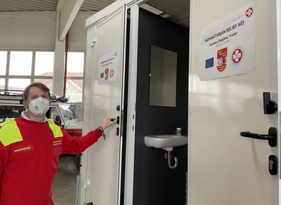 Ein Sanitäts- und Hygienetrailer mit einem Helfer im roten Outfit.