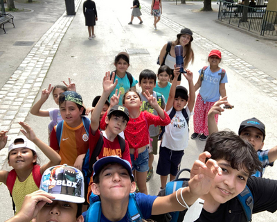 Gruppenfoto von weiter oben aufgenommen, Kinder aus LernLEO in Schönbrunn, tragen sommerliche Outfits, manche tragen Kappen, schauen in Kamera