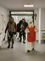Drei Personen in Kostümen, darunter Nikolaus, gehen einen Flur entlang.