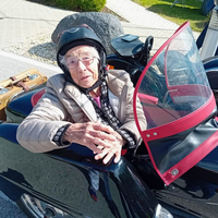 Eine ältere Frau sitzt in einem Motorradseitenwagen und lächelt.