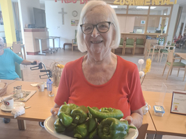 Eine ältere Frau hält einen Teller mit frischen grünen Paprika.