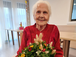 Eine ältere Frau hält einen festlichen Kranz aus Pflanzen und Blumen.