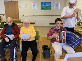 Drei Personen singen und musizieren mit einem Akkordeon in einem Gemeinschaftsraum.