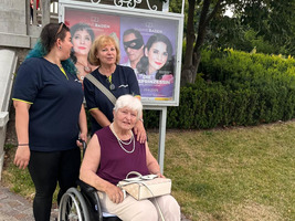 Drei Frauen stehen und sitzen gemeinsam vor einem Plakat für eine Bühnenaufführung.