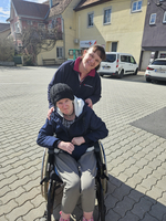 Eine Frau im Rollstuhl wird von einer Pflegekraft freundlich unterstützt.