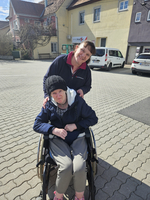 Eine Frau im Rollstuhl wird von einer Pflegekraft freundlich unterstützt.