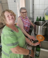 Zwei Frauen füllen mit einem Trichter Wasserflaschen am Spültisch.