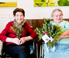 Eine Gruppe älterer Frauen in Rollstühlen hält Blumensträuße.