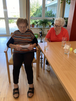 Zwei ältere Frauen sitzen an einem Tisch und lesen gemeinsam Unterlagen.