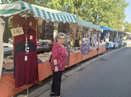 Ältere Frau steht neben Marktständen mit Kleidung und Accessoires.