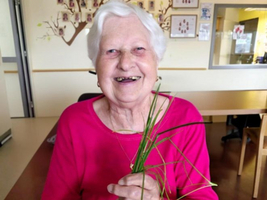 Lächelnde ältere Frau in einem rosa Oberteil hält Gräser in der Hand.