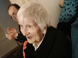 Eine ältere Frau mit weißen Haaren lächelt und applaudiert in einer Gruppe.