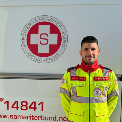 Ein Sanitäter in Uniform steht vor einem Rettungsauto des Samariterbundes.