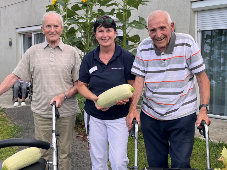 Drei Personen in einem Garten halten eine große Zucchini.