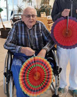 Ein älterer Mann im Rollstuhl hält eine bunte Papierschlange.