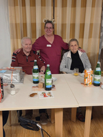Drei Personen sitzen an einem Tisch mit Getränken und Essen.