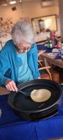 Eine ältere Frau bereitet einen Pfannkuchen in einer großen Pfanne zu.