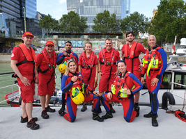 Ein Team von Rettungsschwimmern in rot-blauer Kleidung posiert am Wasser.
