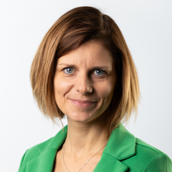 Frau mit blonden, mittellangen Haaren in grünem Blazer lächelt freundlich.