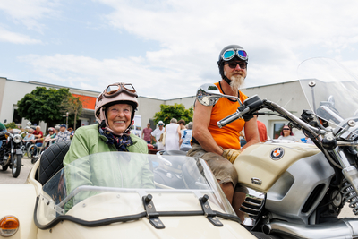 Älteres Paar auf einem Motorrad mit Beiwagen lächelt in die Kamera.