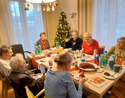 Senioren sitzen gemütlich in weihnachtlichem Wohnzimmer bei Tisch, Weihnachtsfeier, Senioren-WGs