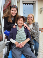 Drei Frauen lächeln freundlich zusammen, eine sitzt im Rollstuhl.