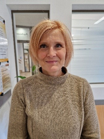 Eine Frau mit blonden Haaren in einem hellen Pullover lächelt freundlich.