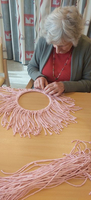 Frau arbeitet an einem handgefertigten Werk aus rosa Wolle.