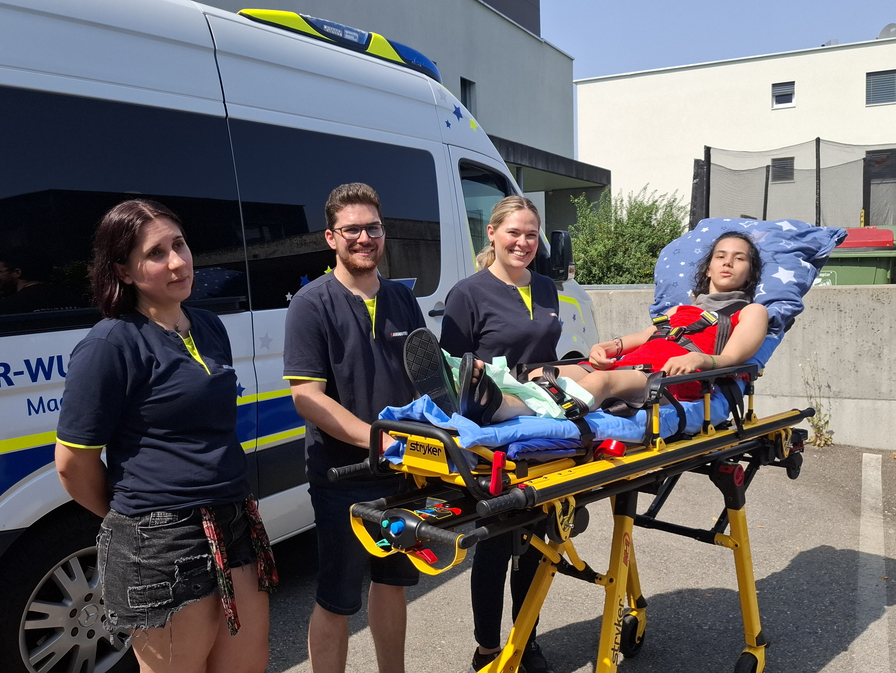 Vier Sanitäter stehen neben einer Trage mit einer Patientin.