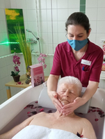 Frau erhält entspannende Gesichtsmassage während eines Bades mit Rosenblättern.