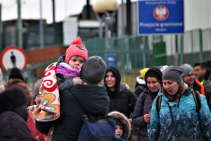 Gruppierung von Menschen an einem Grenzübergang, einige halten Kinder in den Armen.