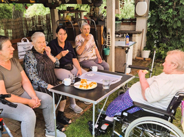 Fünf Frauen genießen Kuchen und Getränke in einem Garten.