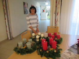Eine Frau steht an einem Tisch mit Weihnachtskränzen und Kerzen.