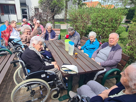 Gruppe älterer Menschen sitzt im Freien zusammen und unterhält sich.