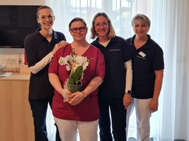 Vier Frauen in Arbeitskleidung, eine hält einen Blumentopf mit Orchideen.
