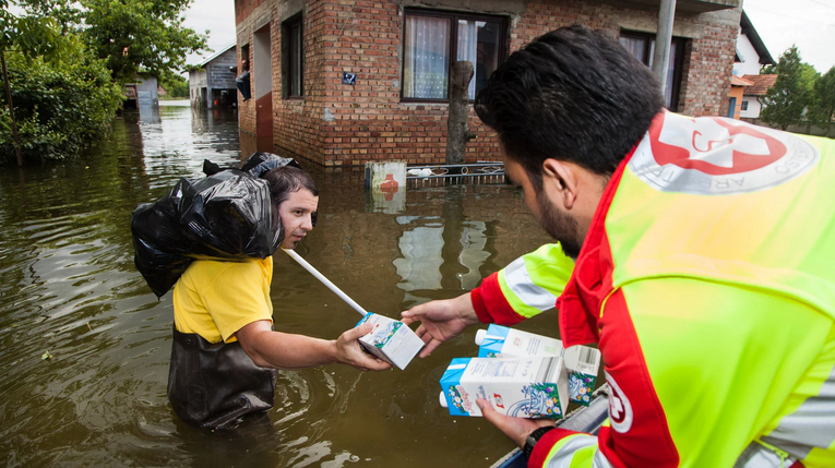 Samariterbund-Mitarbeiter in Boot übergibt Lebensmittel an Person im Hochwasser