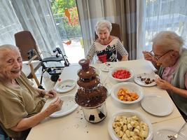 Drei Frauen genießen frisches Obst mit einer Schokoladenfontäne in einem hellen Raum.