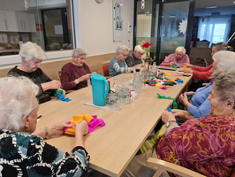 Ältere Frauen basteln gemeinsam mit buntem Papier an einem Tisch.