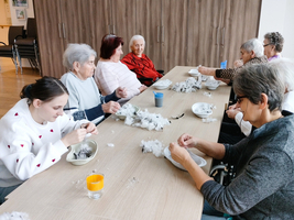 Ältere Menschen und eine junge Frau basteln gemeinsam an einem Tisch.