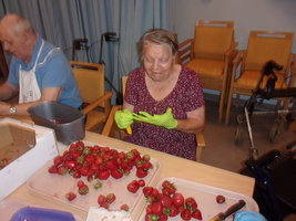 Eine ältere Frau schält Erdbeeren mit grünen Handschuhen am Tisch.