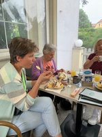 Drei Frauen genießen gemeinsam ein Frühstück mit Eis und Getränken auf einer Terrasse.