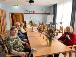 Eine Gruppe älterer Menschen sitzt um einen Tisch mit dekorierten Osterzweigen.