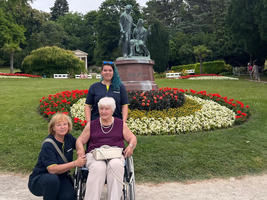 Drei Frauen, eine im Rollstuhl, posieren vor einer Statue im Park.